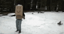 a man wearing a cardboard box with a smiley face on it is standing in the snow .