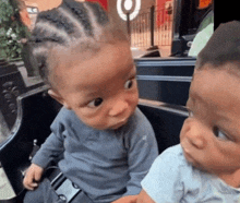 two babies are sitting next to each other and one has a braided head