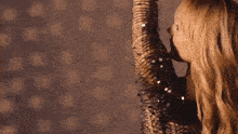 a woman in a sequined dress is standing in front of a wall with her arms in the air .