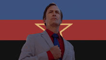 a man in a suit and tie stands in front of a flag with a red star on it