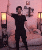 a man wearing headphones stands in a living room with his arms in the air