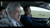 three men are sitting in a car with the word arte on the bottom