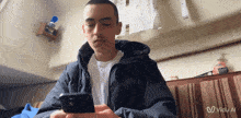 a man in a black jacket is looking at his cell phone with a vidu al logo behind him