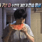 a man is eating a watermelon in front of a wall with chinese writing