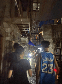 a man wearing a jordan 23 jersey walks down a narrow alleyway