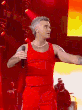 a man in a red tank top sings into a microphone on a stage