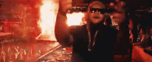 a man wearing sunglasses is standing in front of a crowd with his arms up in the air .
