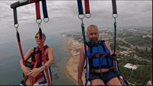a man and a woman are flying in a parachute over the ocean