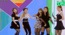 a group of women are dancing in front of a sign that says toko on it