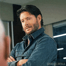 a man with a beard is wearing a denim shirt with his arms crossed