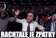 a man wearing headphones and a tie stands in front of a crowd and says bachtale je zaptky