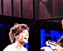a man laughs while playing a guitar in front of a sign that says ' nirvana '