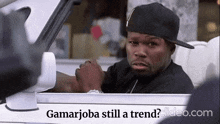 a man in a black hat is sitting in a car with the words gamarjoba still a trend