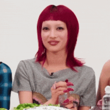 a woman with red hair and long nails is sitting at a table with a bottle of water .