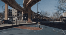 a woman is playing basketball under a bridge in a park