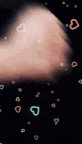 a person 's hand is surrounded by colorful hearts on a dark background