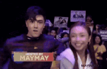 a man and a woman are standing next to each other with a sign that says hosted by maymay on it