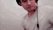 a man wearing glasses and a hat with a microphone on his head is standing in front of a white wall .