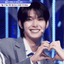 a young man in a suit and tie making a heart shape with his hands