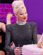 a drag queen is wearing a black and white polka dot dress and holding a pink cotton candy .
