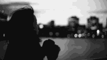 a black and white photo of a woman taking a picture of a city at night .