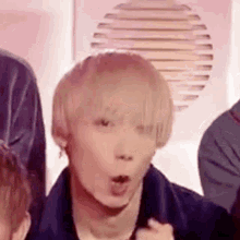 a young man with blonde hair is making a funny face while standing next to a group of people .