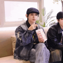 a man sitting on a couch eating popcorn from a cup that says popcorn on it