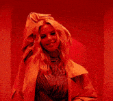 a woman in a yellow jacket is standing in front of a red wall and smiling .