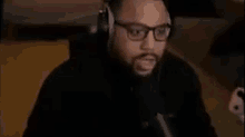 a man wearing glasses and headphones is sitting in front of a microphone .