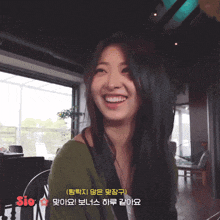 a woman in a green sweater is smiling in front of a sign that says ' sio ' on it