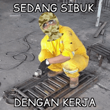 a man wearing a camouflage mask is kneeling down using a grinder and the words sedang sibuk dengan kerja are above him