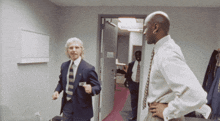 a man in a suit and tie is standing next to another man in a white shirt and tie