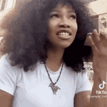 a woman with curly hair is wearing a white t-shirt and a necklace with a horse pendant .