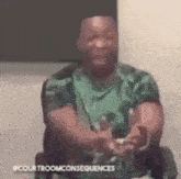 a man in a green shirt is sitting in a chair and holding a remote control .