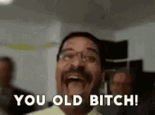 a man with glasses is laughing and saying you old bitch .