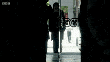 a woman in a black coat is standing in front of a glass door with bbc written on it