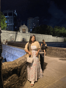 a woman in a white dress is standing in front of a stone wall at night