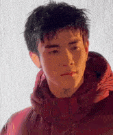 a young man is wearing a red jacket with a hood and looking at the camera .