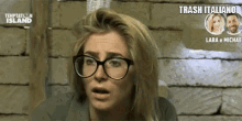 a woman wearing glasses looks shocked in front of a temptation island poster