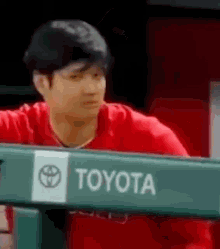 a man in a red shirt is leaning over a fence with a toyota logo on it .