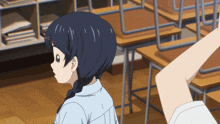 a girl in a blue shirt is standing in front of a classroom with empty desks