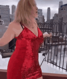 a woman in a red dress is dancing on a balcony with a city in the background .