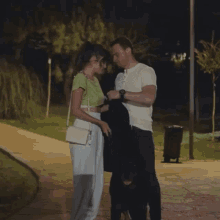 a man adjusts a woman 's jacket while they walk down a sidewalk