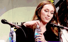 a woman is sitting at a table holding a bottle of water and talking into a microphone .