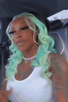a woman with green hair is sitting in a car wearing a white tank top .