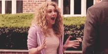 a woman with curly hair is standing next to a man with her mouth open and a surprised look on her face .