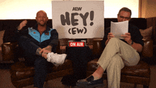 two men sit on a couch with a sign that says hey