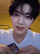 a young man in a white shirt is holding a pokemon card in his hand .