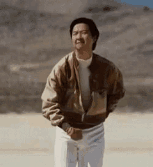 a man in a jacket and white pants is standing in a desert .