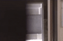 a person is standing in a dark room looking out of a window .